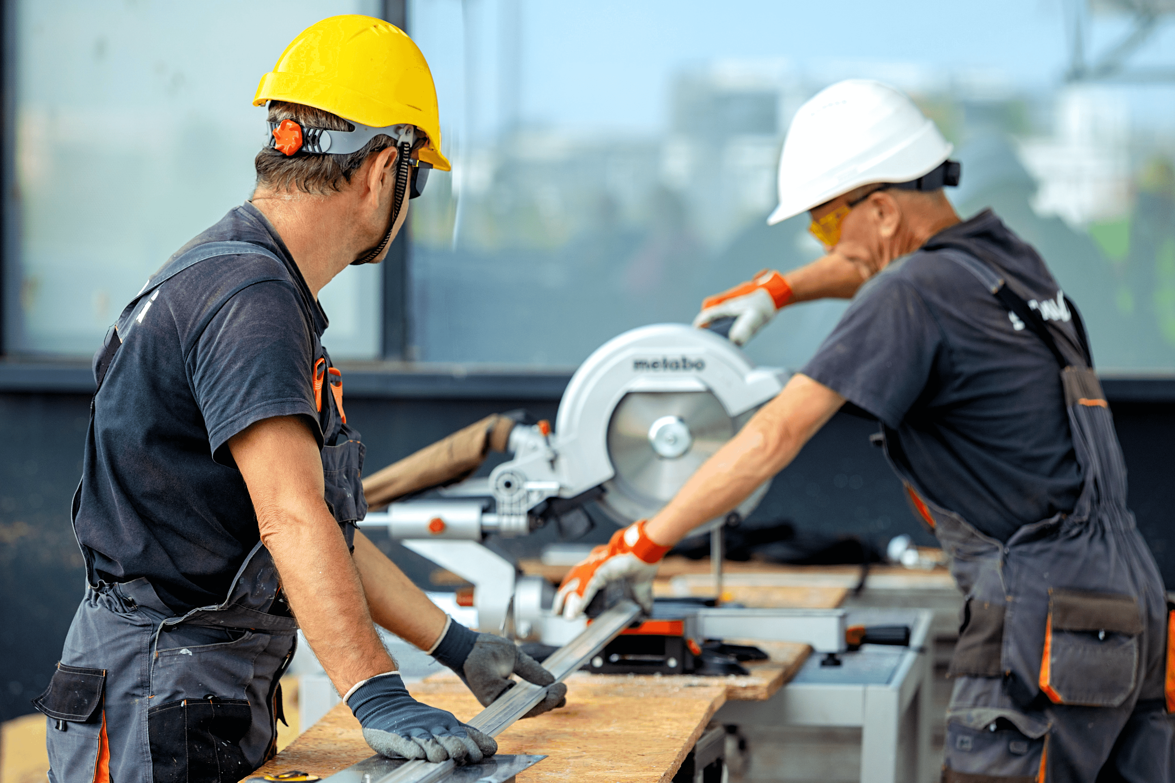 two men in hard hats operating a table saw