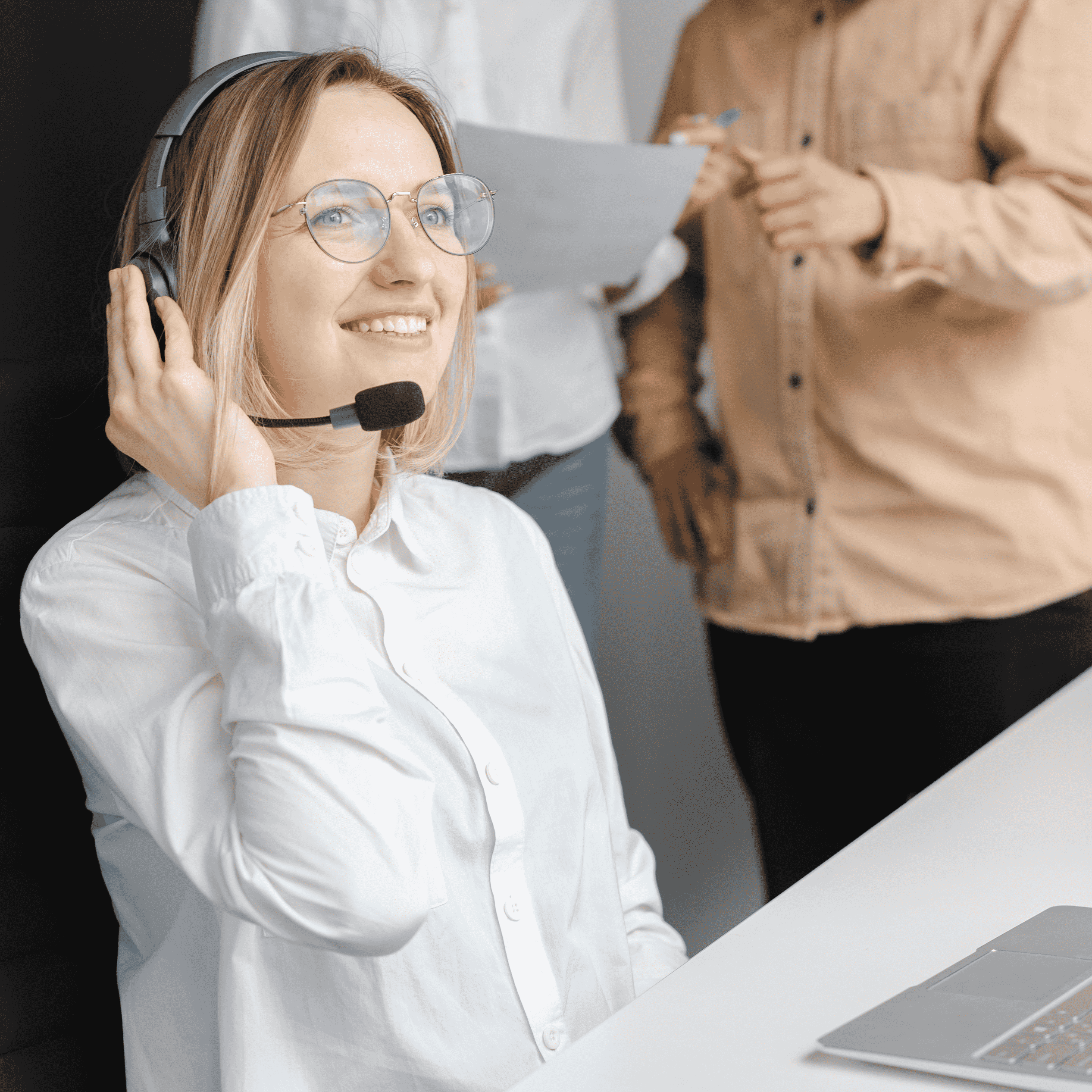 lady in a white button-up shirt with headset. Two people behind her looking at a document.